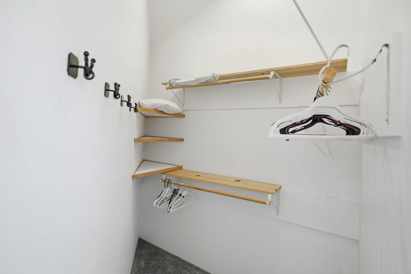 Walk-in closet with white walls, carpeted floor, built-in wooden shelves, hanging rods, and wall hooks.
