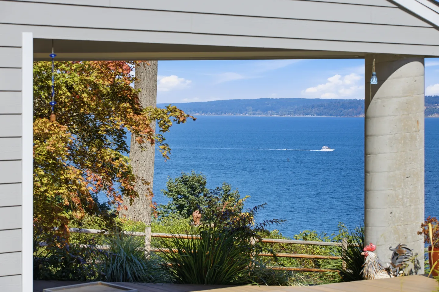 View of blue water and distant hills framed by an outdoor deck structure and concrete pillar.