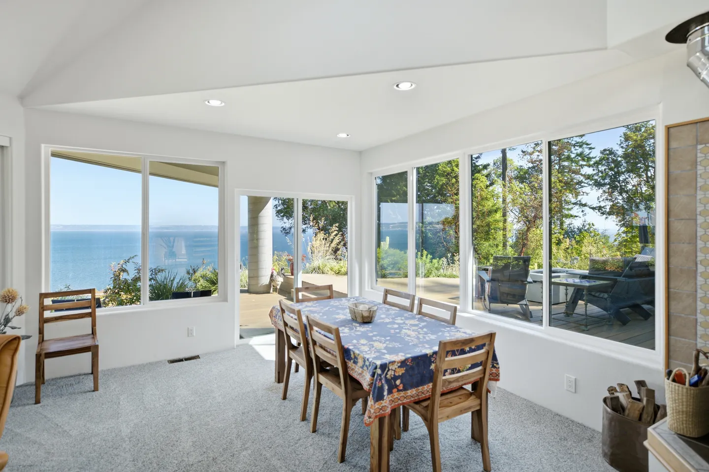 Dining area with a patterned tablecloth on the table, surrounded by large windows showing ocean and outdoor deck views.