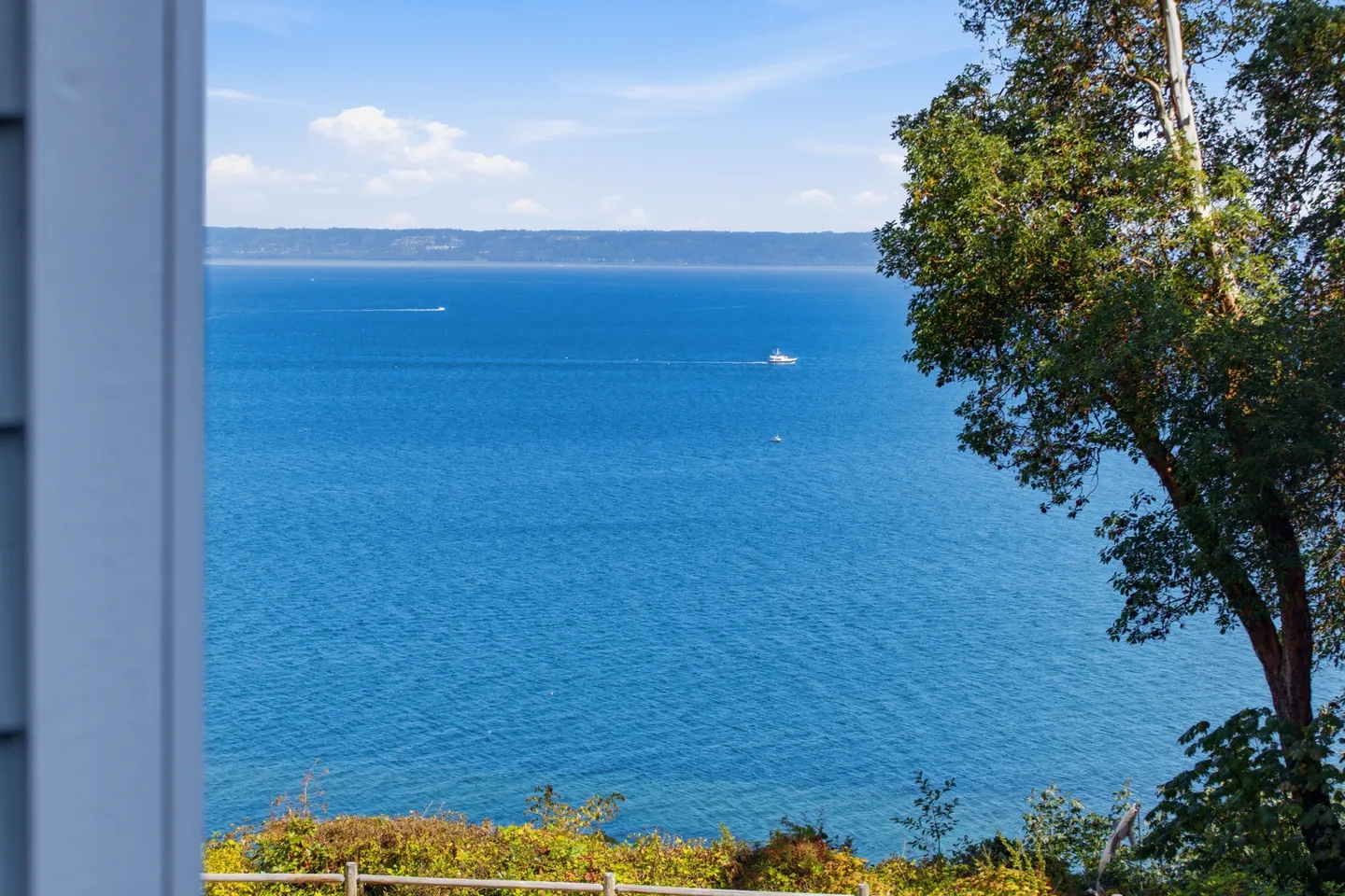 Elevated outdoor view of a wide blue body of water under a clear sky, framed by trees and an exterior wall.