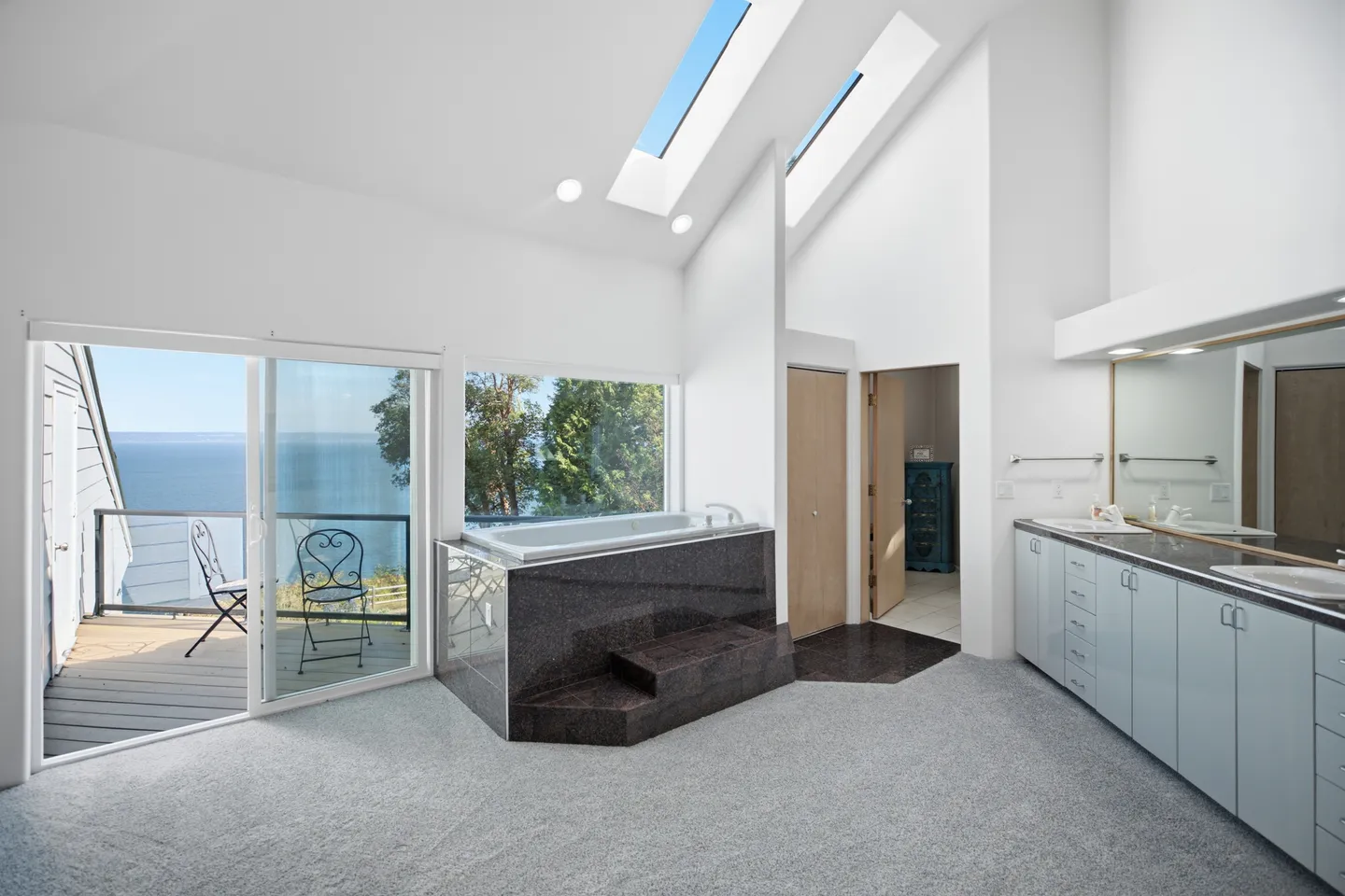 Bathroom with high vaulted ceilings, skylights, a raised platform jetted tub, and sliding glass doors opening to a balcony with water views.