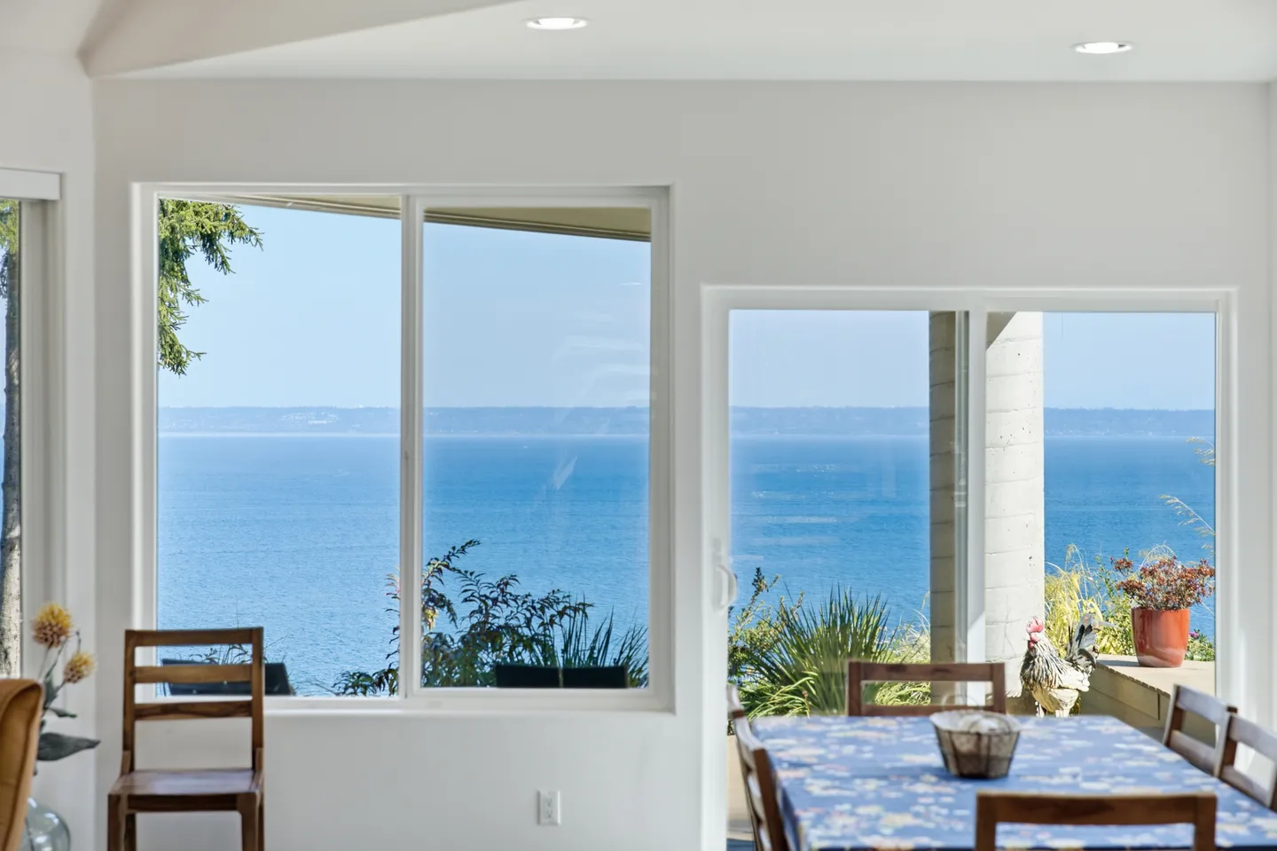 Indoor dining area with large windows and a glass door looking out toward a blue ocean under a clear sky.