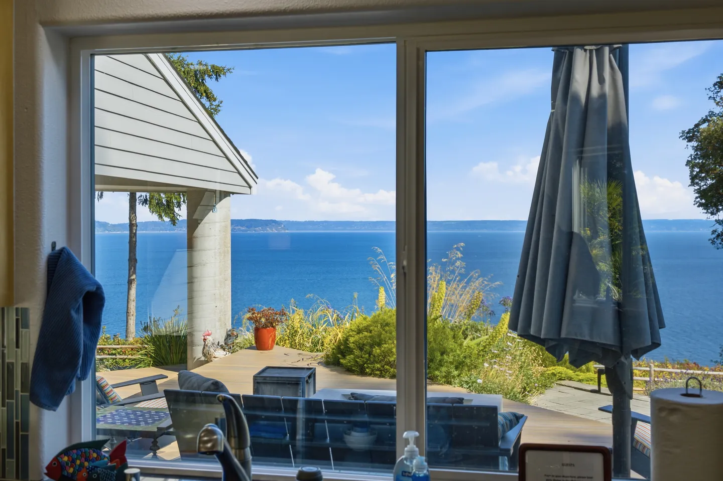 A large indoor window looking out onto an outdoor patio and wide blue water views under a clear sky.