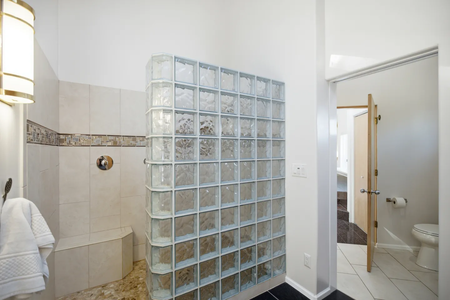 Walk-in shower with a glass block partition wall, tiled bench, and an adjoining toilet room.