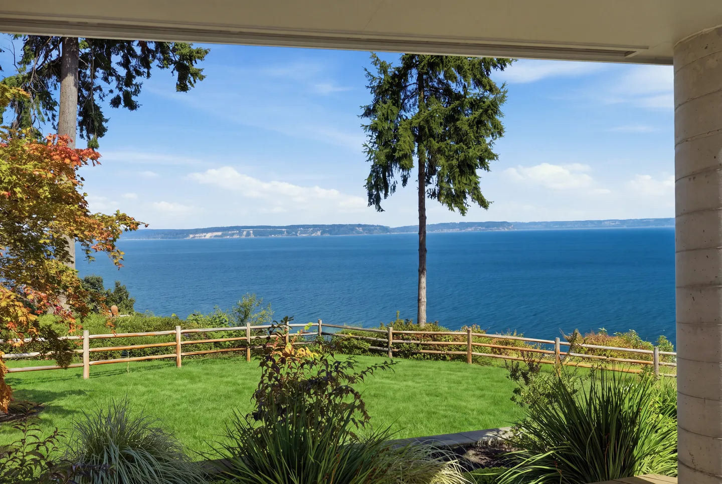 View of a green lawn and wide blue water from a covered porch or patio.
