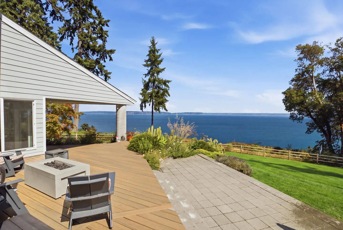 Outdoor deck and patio with a fire pit table, chairs, lawn, and an expansive view of the open water.