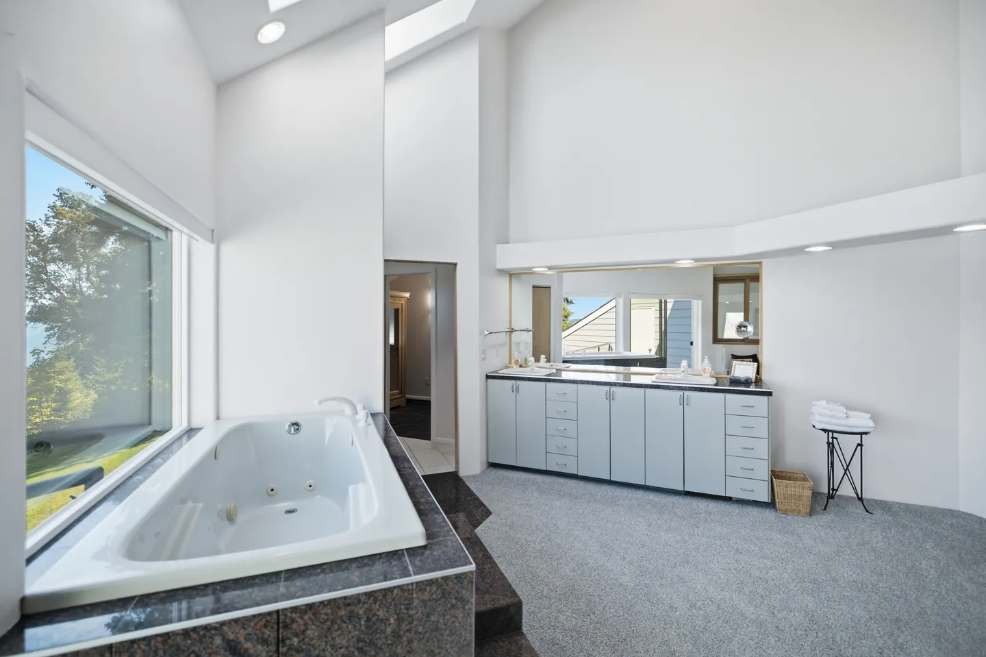 Spacious bathroom featuring a sunken jetted bathtub next to a large window and a long double vanity with mirrors.