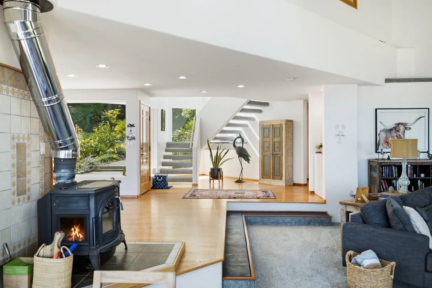 Open-concept living space with a wood-burning stove, sunken carpeted living area, and stairs leading to the upper level.