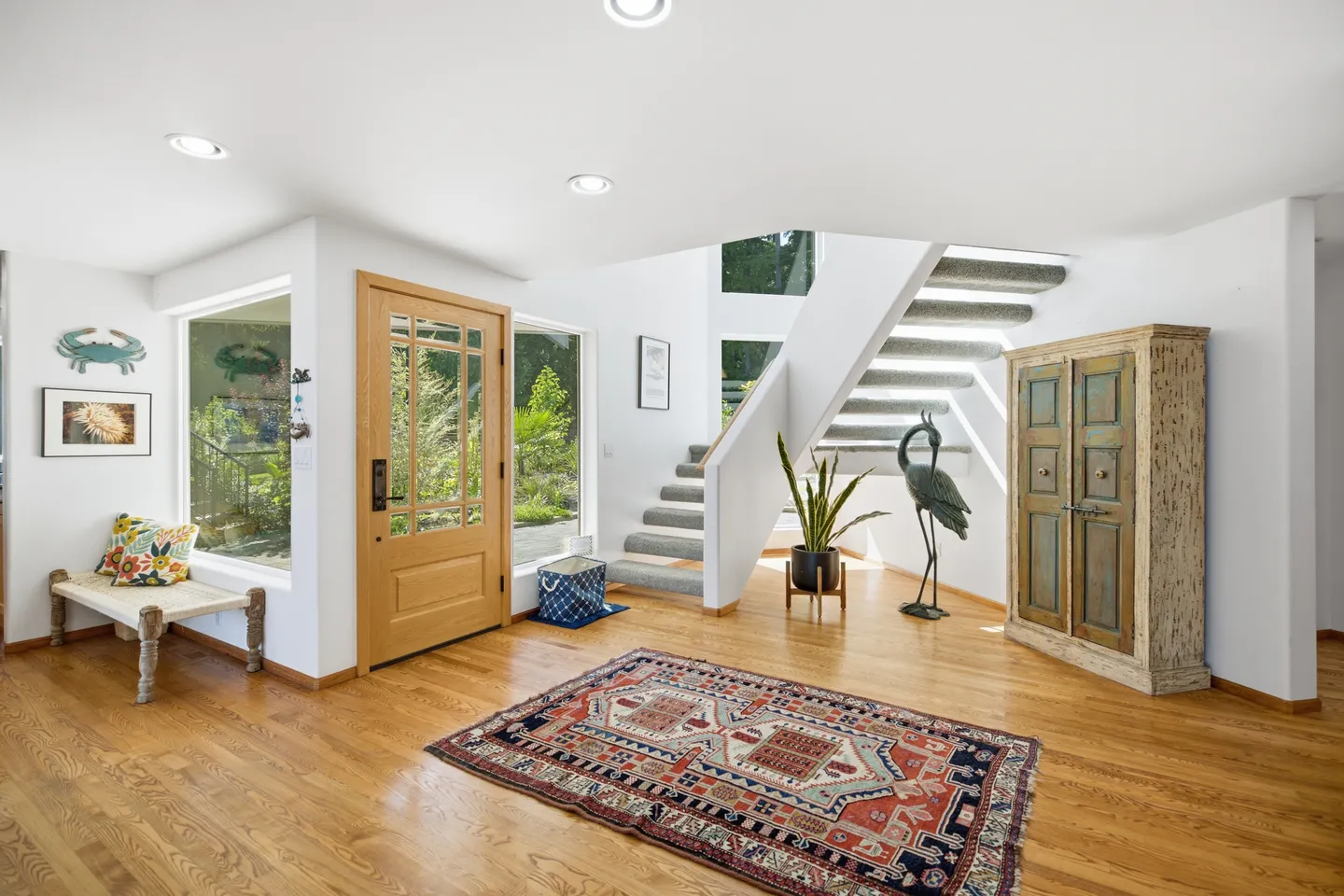 Bright entryway featuring a wooden front door with glass panes, wood flooring, a patterned area rug, and carpeted stairs leading up.