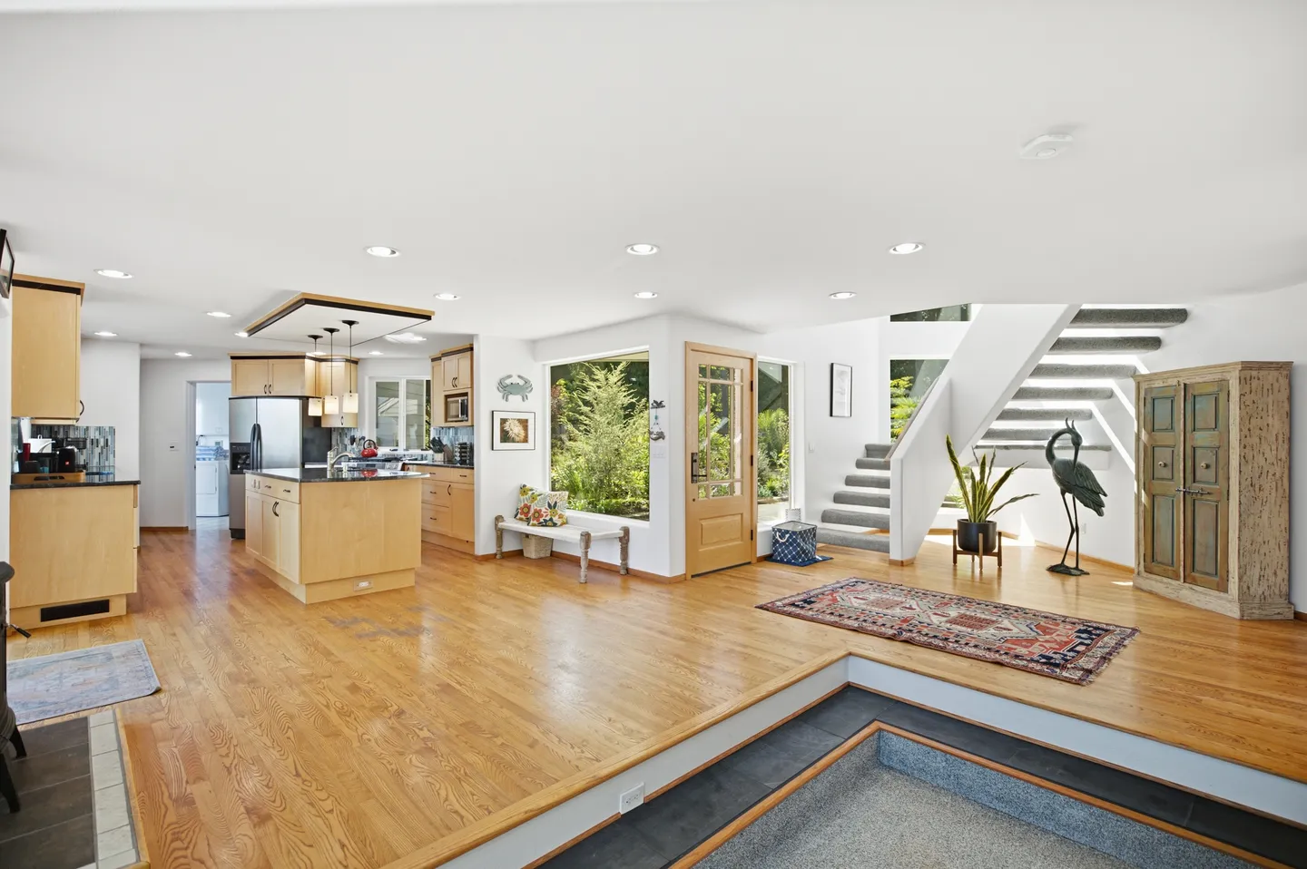 Open-concept entryway and kitchen featuring hardwood flooring, an island with pendant lighting, and a sunken living room area.