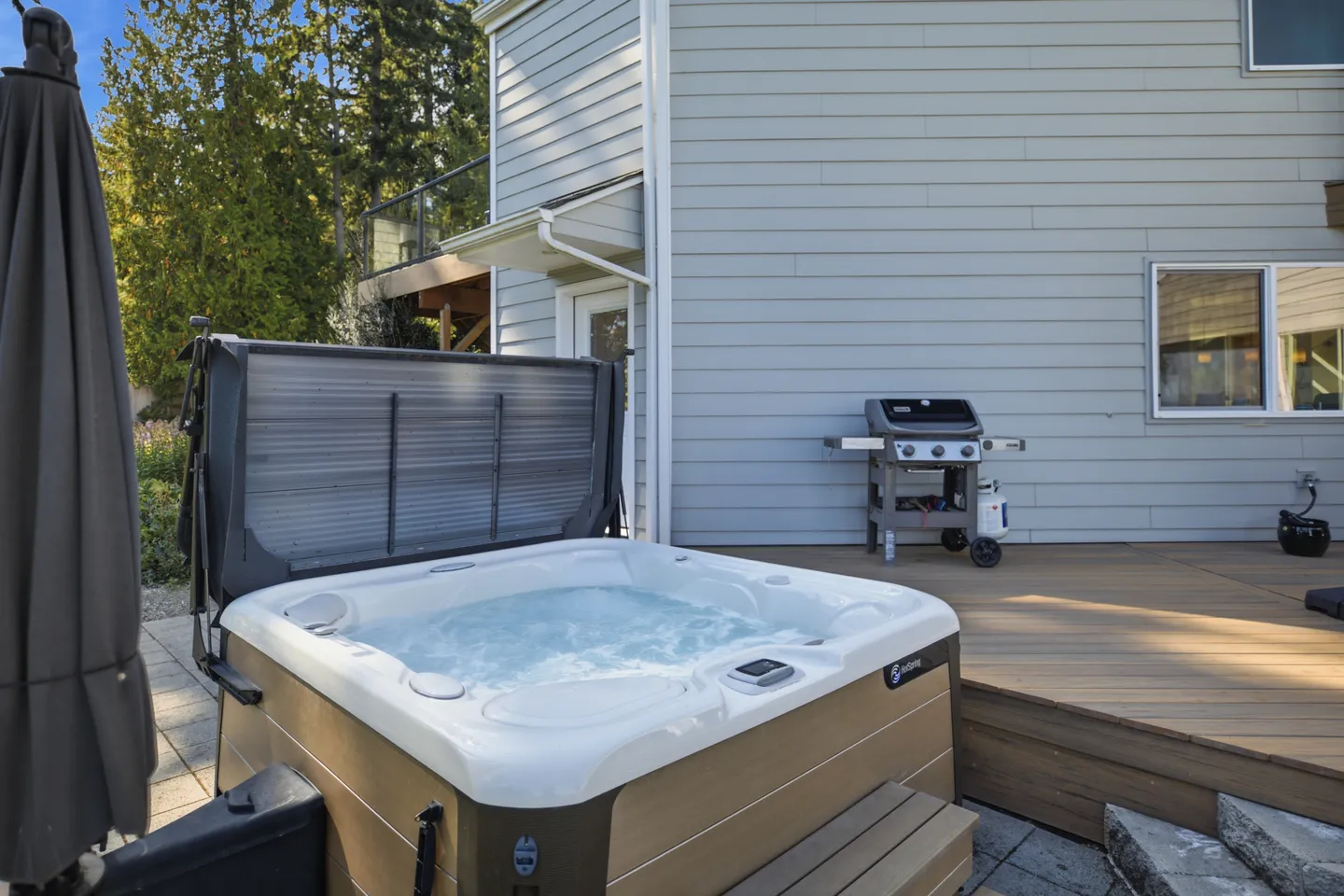 Outdoor hot tub with bubbling water next to a raised wooden deck with a barbecue grill.