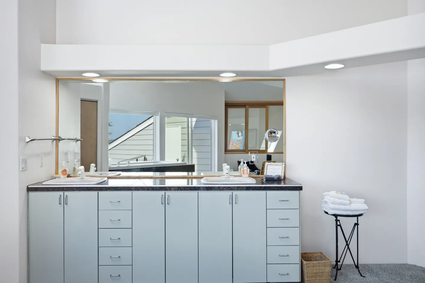 Bathroom vanity with two sinks, a wide mirror, light blue cabinets, and recessed lighting overhead.