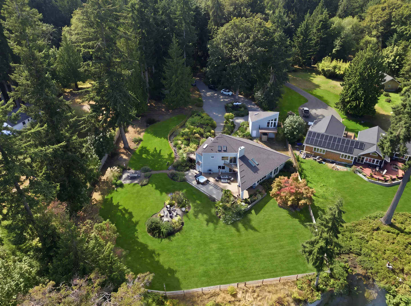 Aerial view of a multi-story home surrounded by expansive green lawns, mature evergreen trees, and outdoor patio spaces.