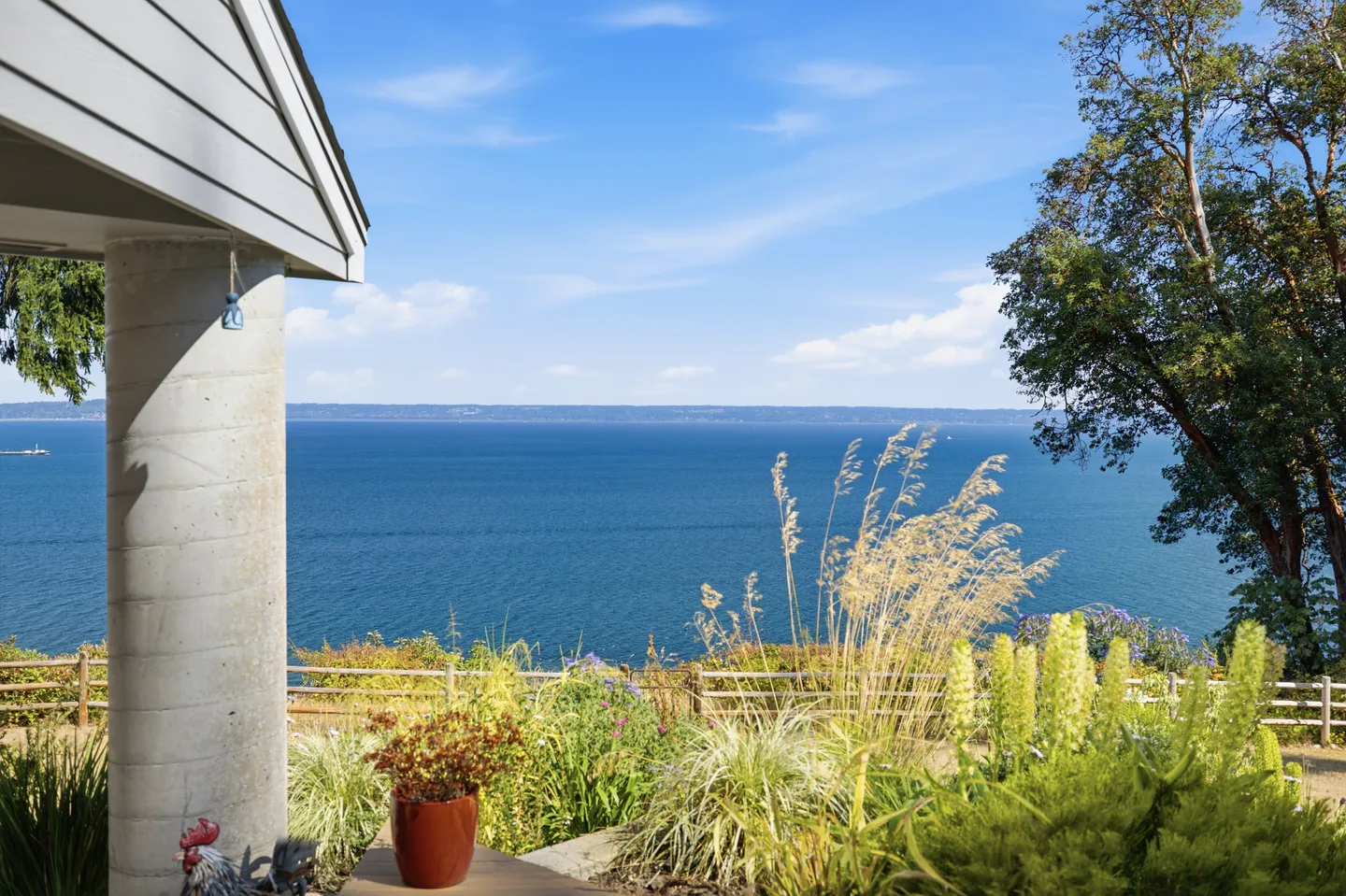 Outdoor patio view overlooking a large blue body of water under a sunny sky with native grasses and plants in the foreground.