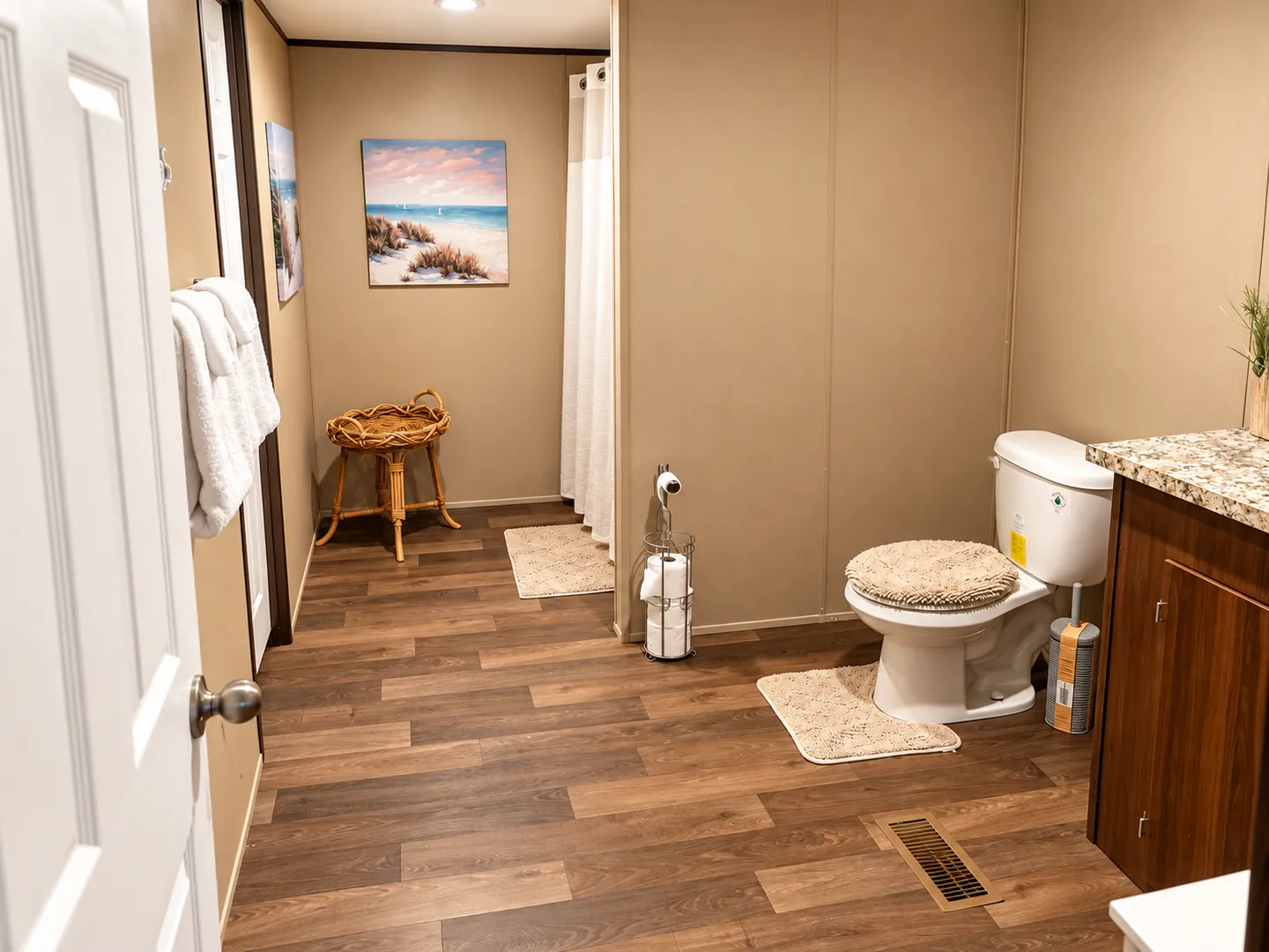 Bathroom with wood-look flooring, a toilet, a vanity counter, a small woven basket stand, and a shower area visible in the background.