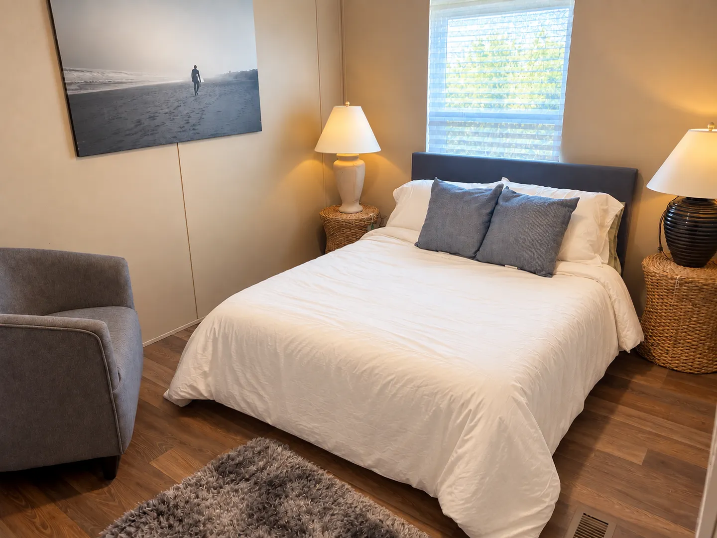Bedroom featuring a made bed with white linens and blue accent pillows, flanked by wicker nightstands with lamps.
