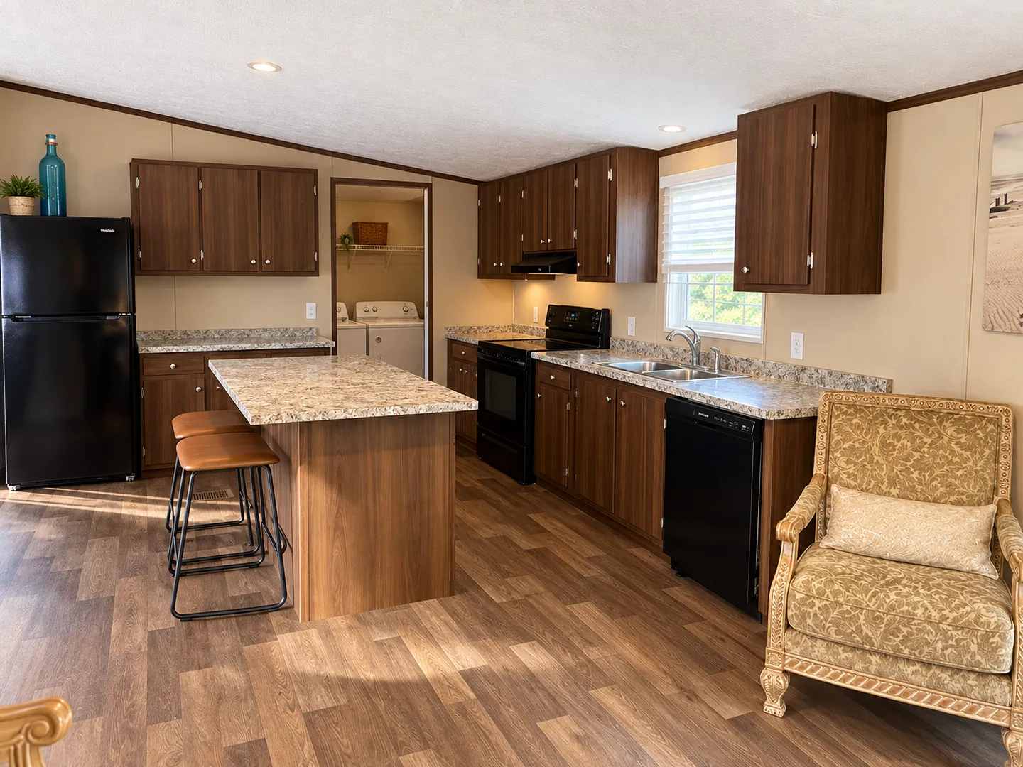Kitchen with wood-grain cabinets, speckled countertops, kitchen island with barstools, black appliances, and view into the laundry room.