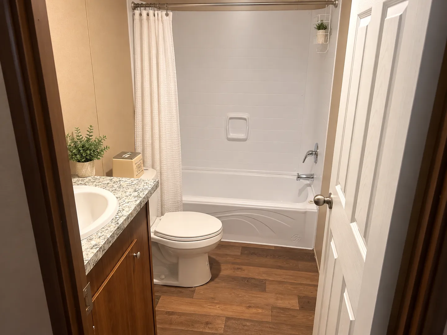 Bathroom with a white bathtub and shower combination, toilet, vanity with speckled countertop, and wood-look flooring.