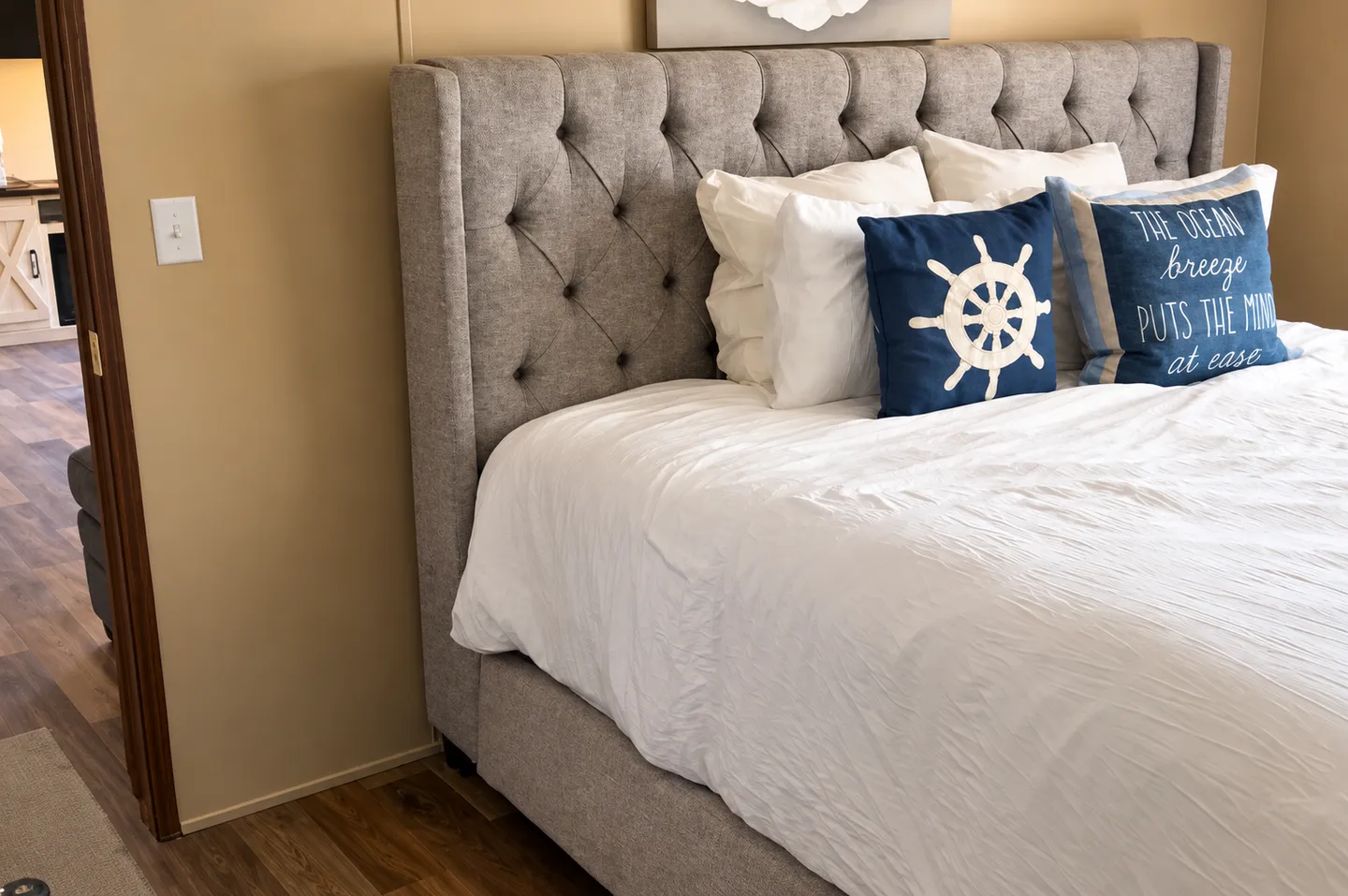Close-up of a bed with a gray tufted headboard, white bedding, and nautical accent pillows.