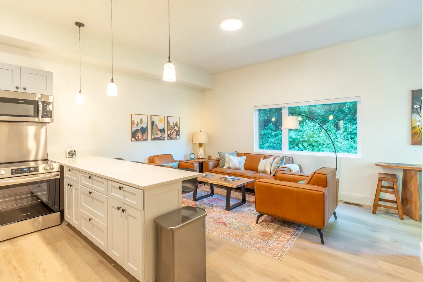 Open-concept living and kitchen area featuring light cabinetry, a kitchen island, and brown leather seating around a coffee table.
