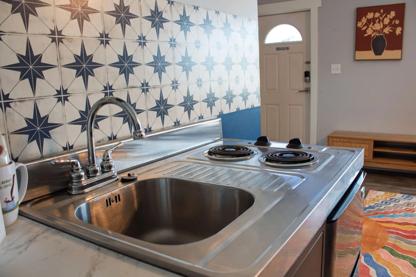 Close-up of a stainless steel sink and two-burner cooktop against a star-patterned tile backsplash.