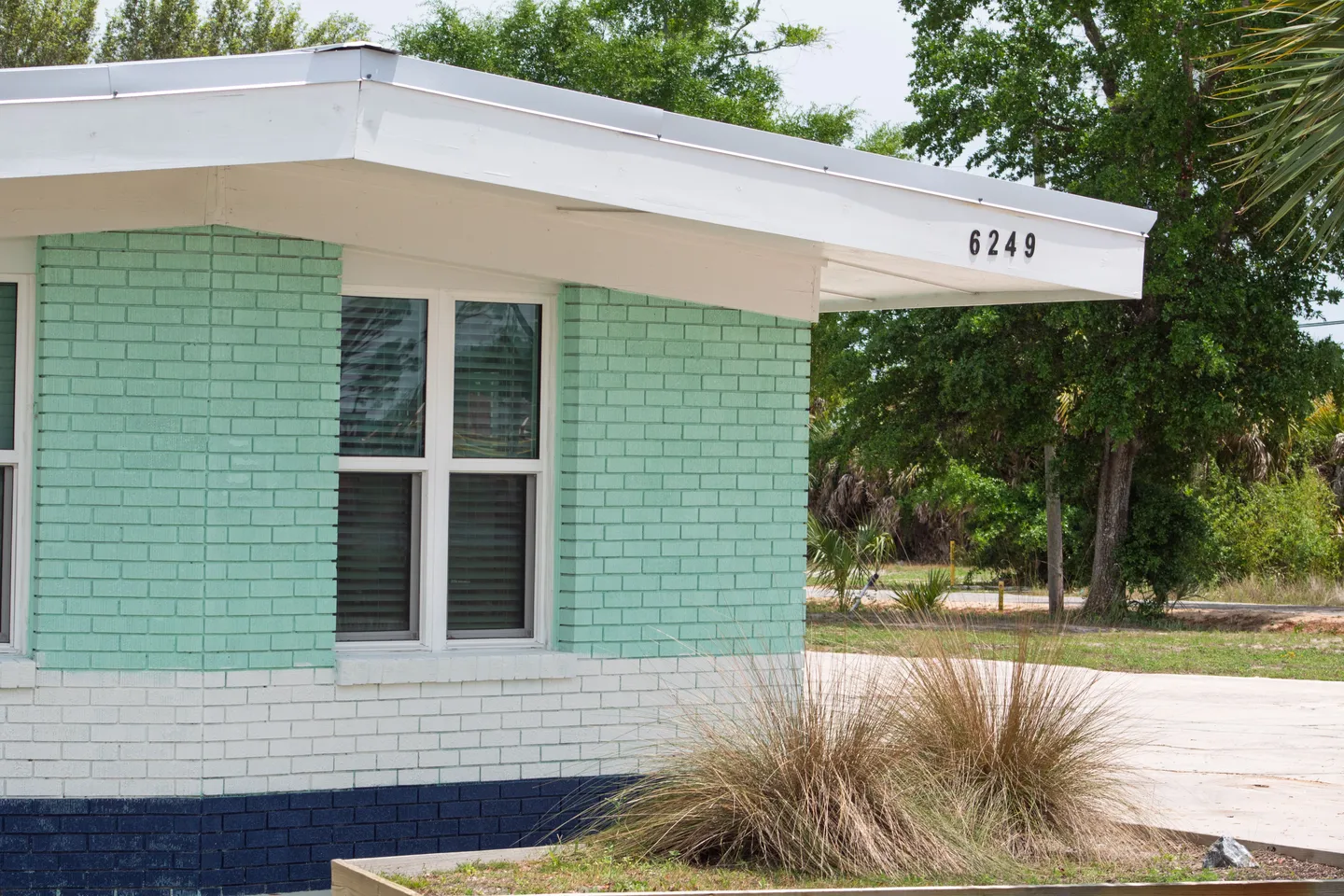 Exterior corner of a painted brick home with a white roof overhang displaying house number 6249.