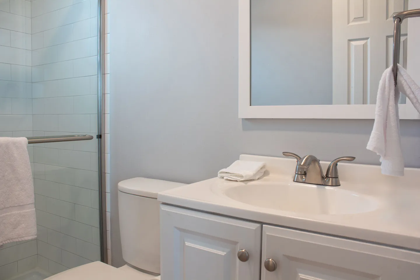 Bathroom with white vanity, framed mirror, toilet, and glass-door tiled shower.