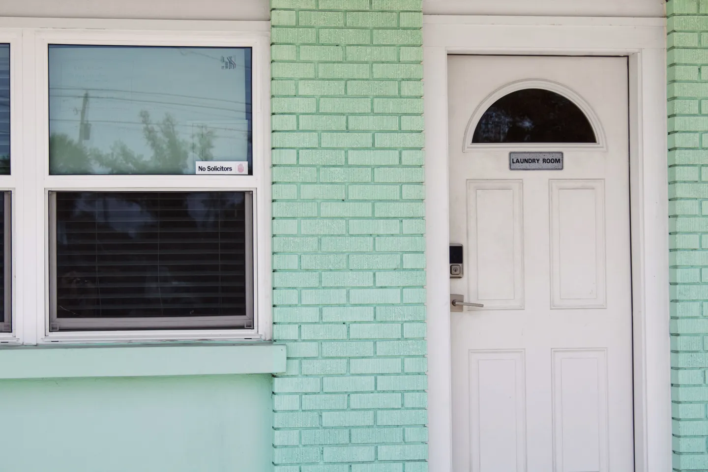Exterior mint green brick wall featuring a window and a white door labeled Laundry Room.
