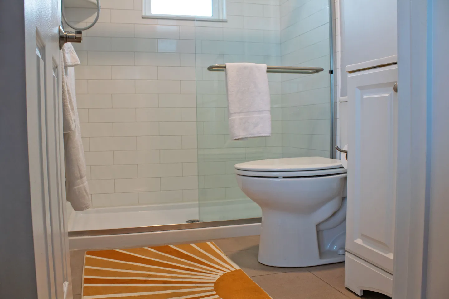 Bathroom with white tiled walk-in shower, glass sliding door, toilet, and a vanity cabinet.