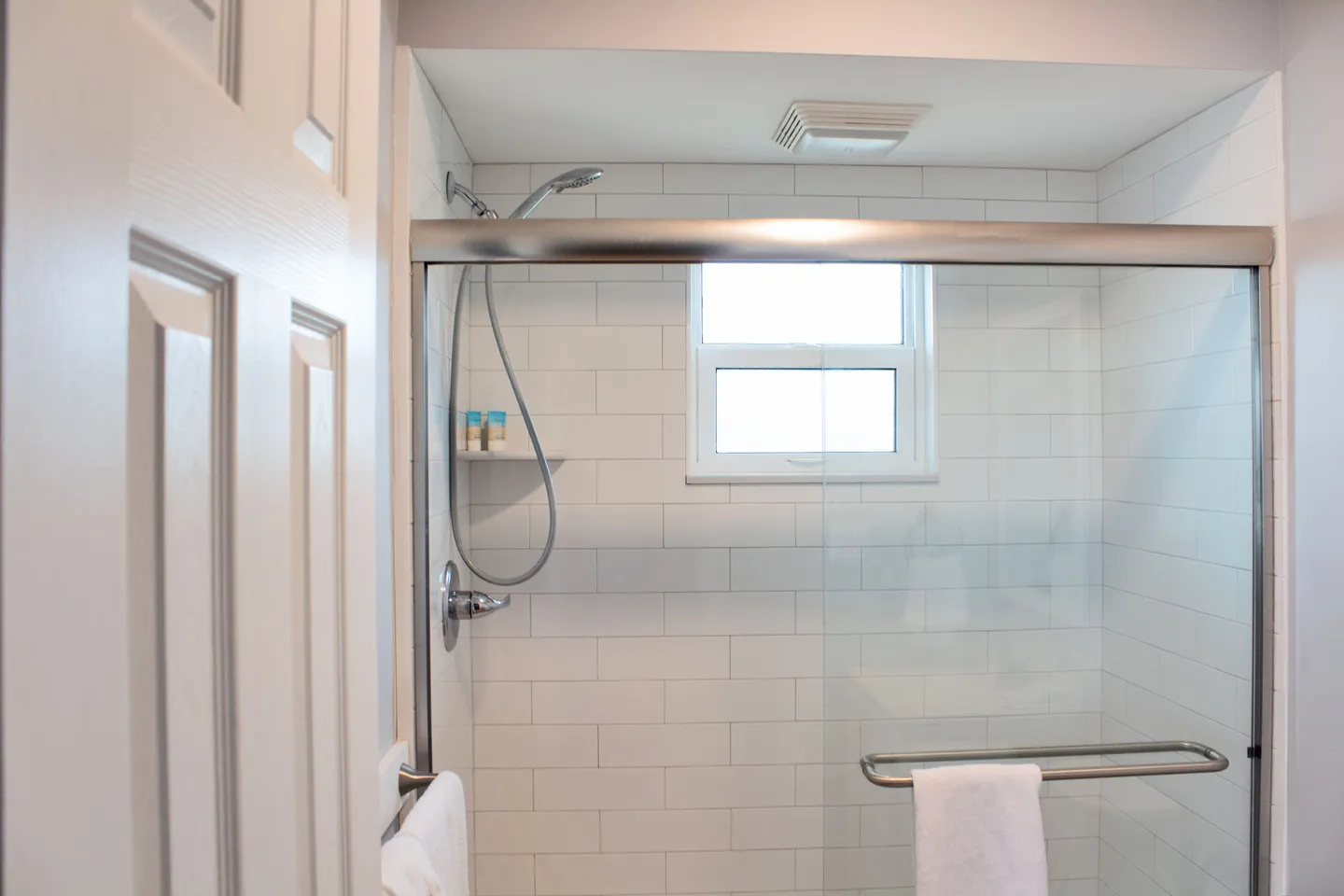 Bathroom walk-in shower with white subway tile, sliding glass doors, a window, and a handheld showerhead.