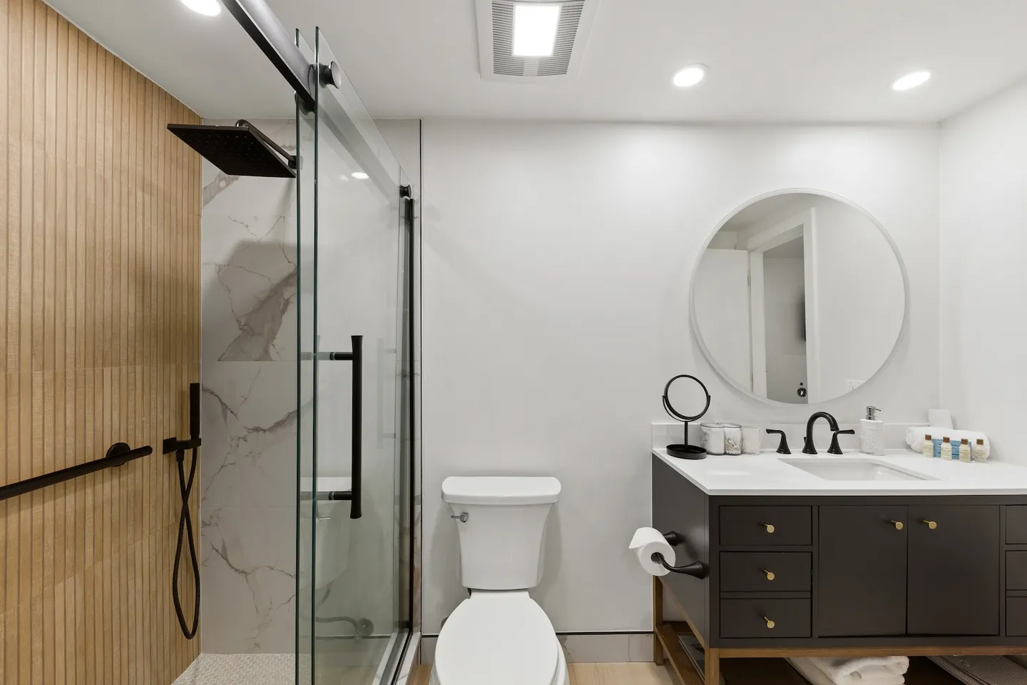 Modern bathroom featuring a glass-enclosed walk-in shower, white toilet, and a vanity with a circular mirror.