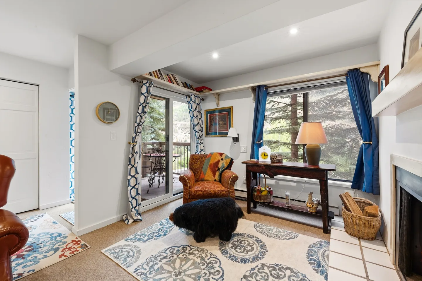 Living room nook with an armchair, bear-shaped ottoman, console table, fireplace edge, and sliding glass door leading to a balcony.