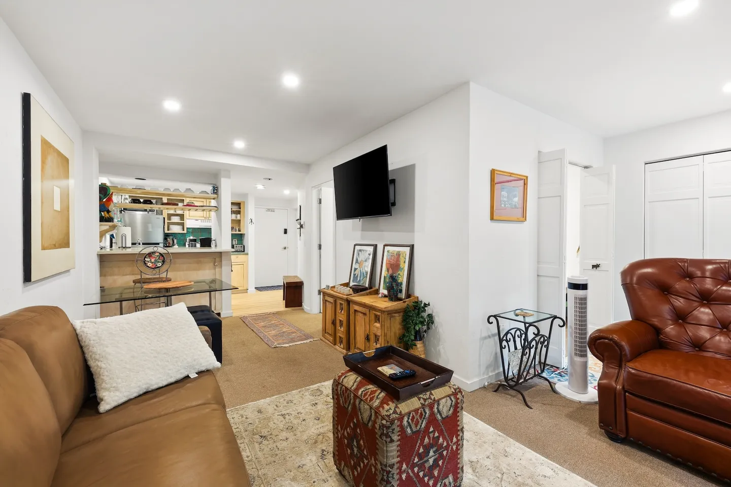 Living room area looking past leather seating and a TV toward a breakfast bar and kitchen.