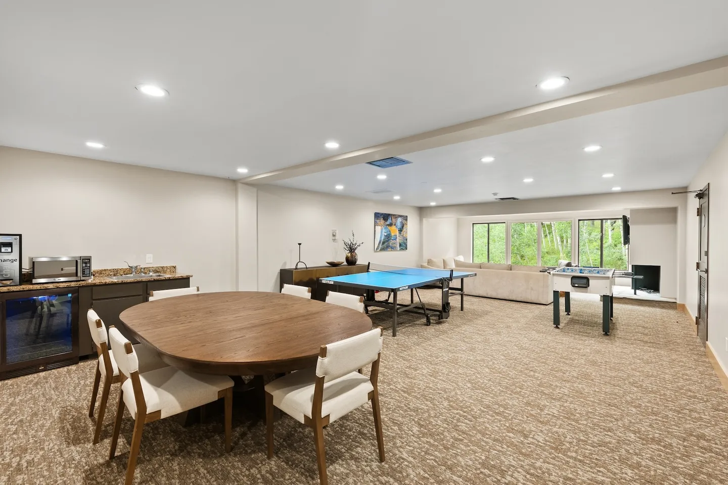 Game room and lounge featuring a ping pong table, foosball table, round dining table, wet bar, and sofa area by large windows.