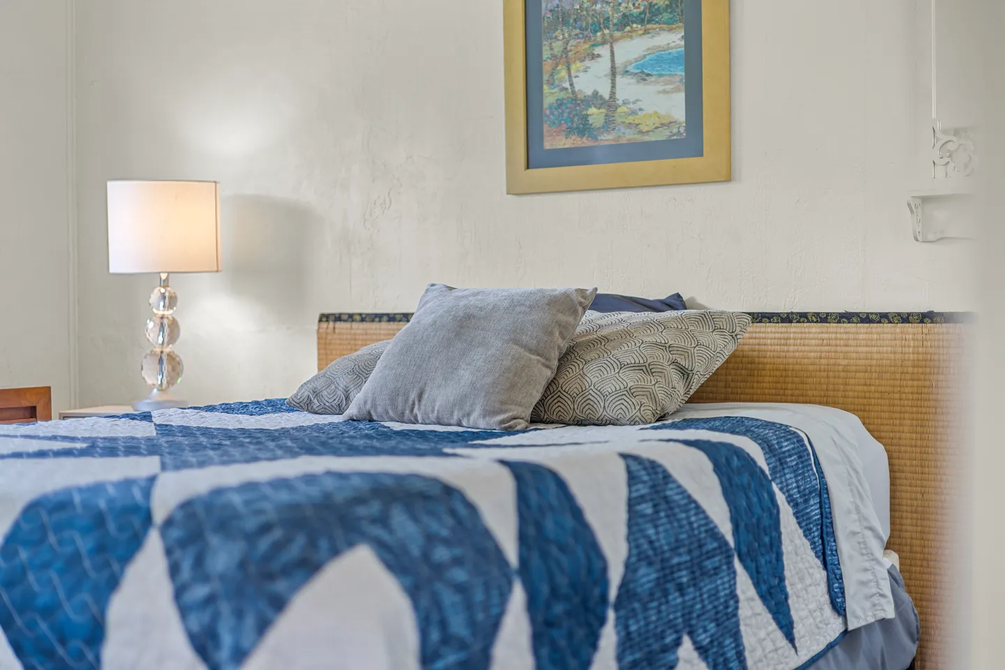 Close-up view of a made bed featuring a blue and white patterned quilt, woven headboard, and a bedside lamp with stacked glass globes.