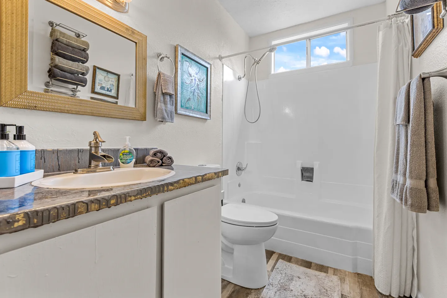 Bathroom featuring a vanity with an oval sink, a toilet, and a bathtub shower combination with a small high window.