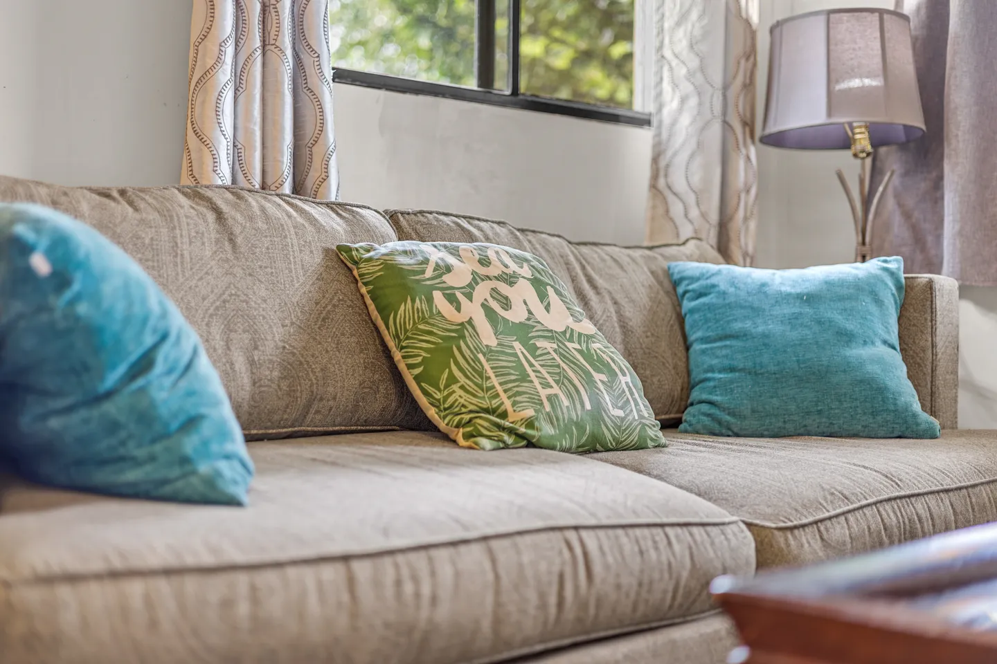 Close-up of a neutral fabric sofa with teal and green patterned accent pillows in a living room.
