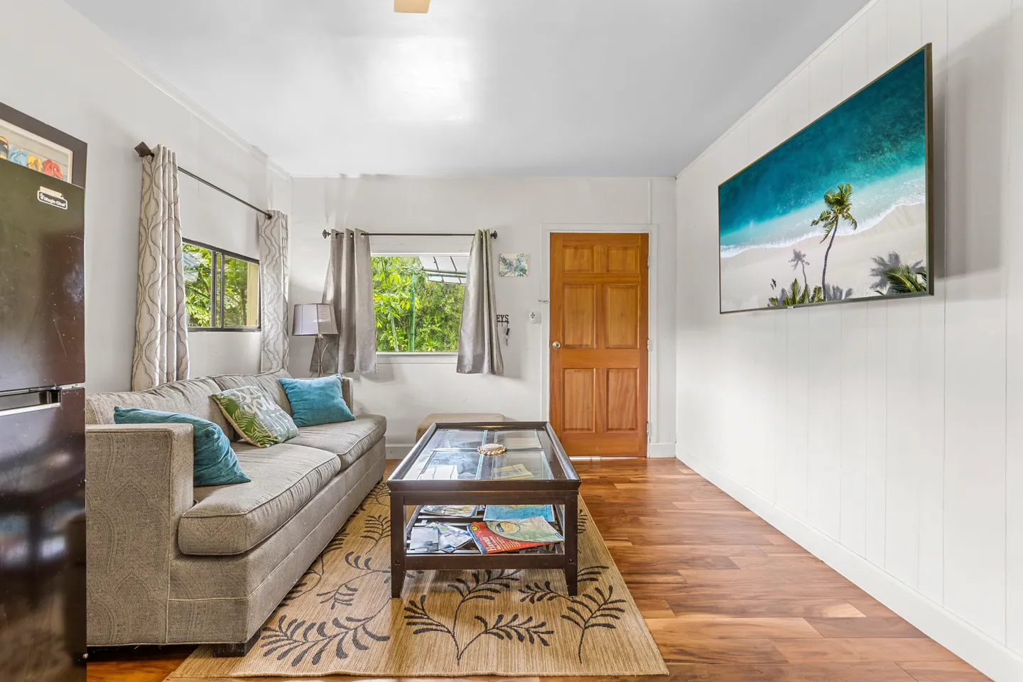 Living room featuring a grey couch, glass-top coffee table on an area rug, wood-look flooring, and a wall-mounted flat-screen television.