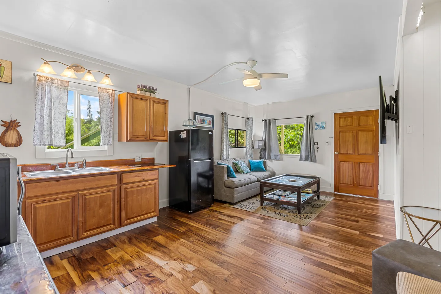 Open-concept living and kitchen area featuring wood flooring, warm-toned cabinets, and a living area with a sofa and coffee table.