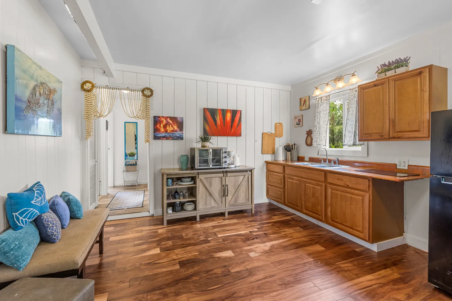 Kitchenette and sitting area featuring wooden floors, white paneled walls, wood cabinets, a sink, and a cushioned bench.
