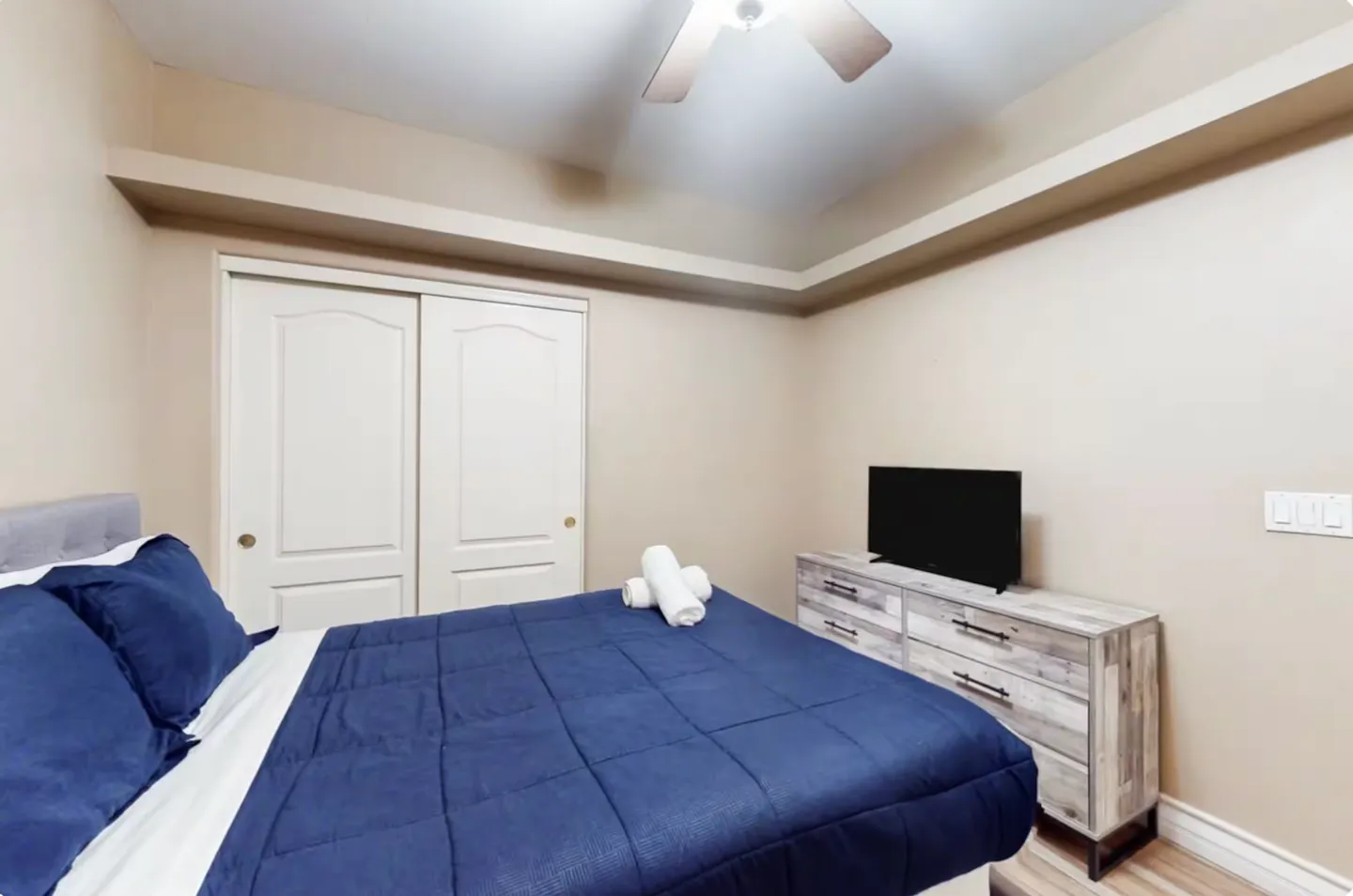 Bedroom featuring a bed with a navy blue comforter, rolled towels, a modern dresser with a television, and a sliding closet door.