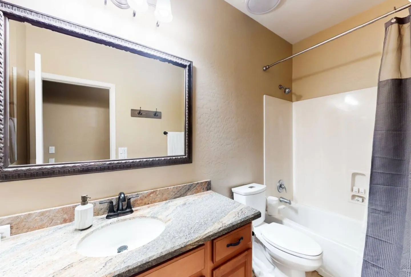 Bathroom with a granite-style countertop vanity, large framed mirror, toilet, and shower-tub combination.