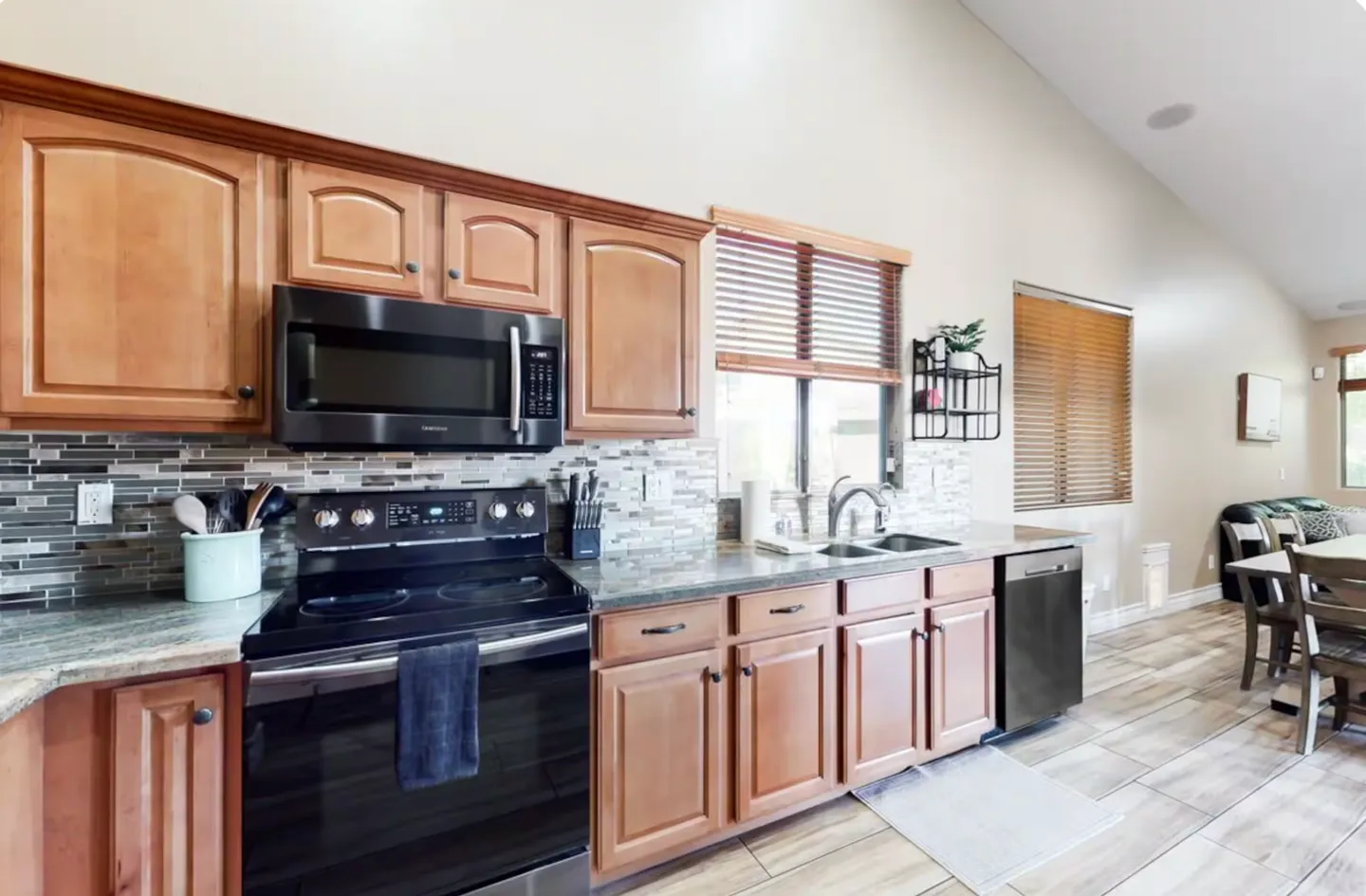 Kitchen counter and cabinets featuring black appliances, tiled backsplash, and an adjoining dining and living area.