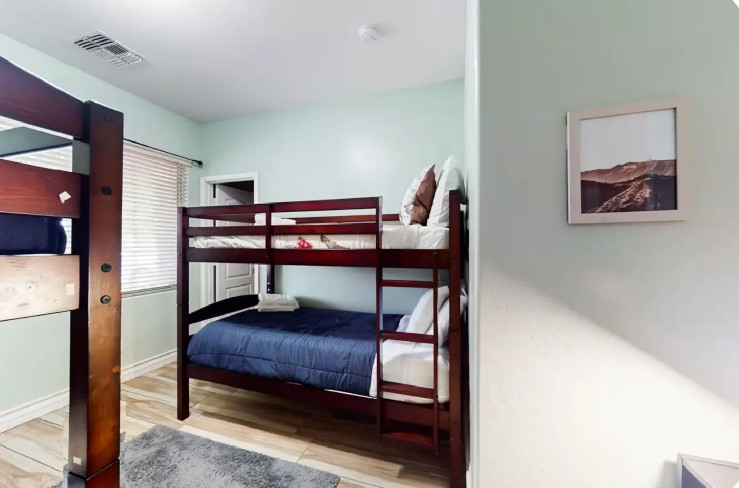 Bedroom with light green walls and dark wood bunk beds with blue bedding.