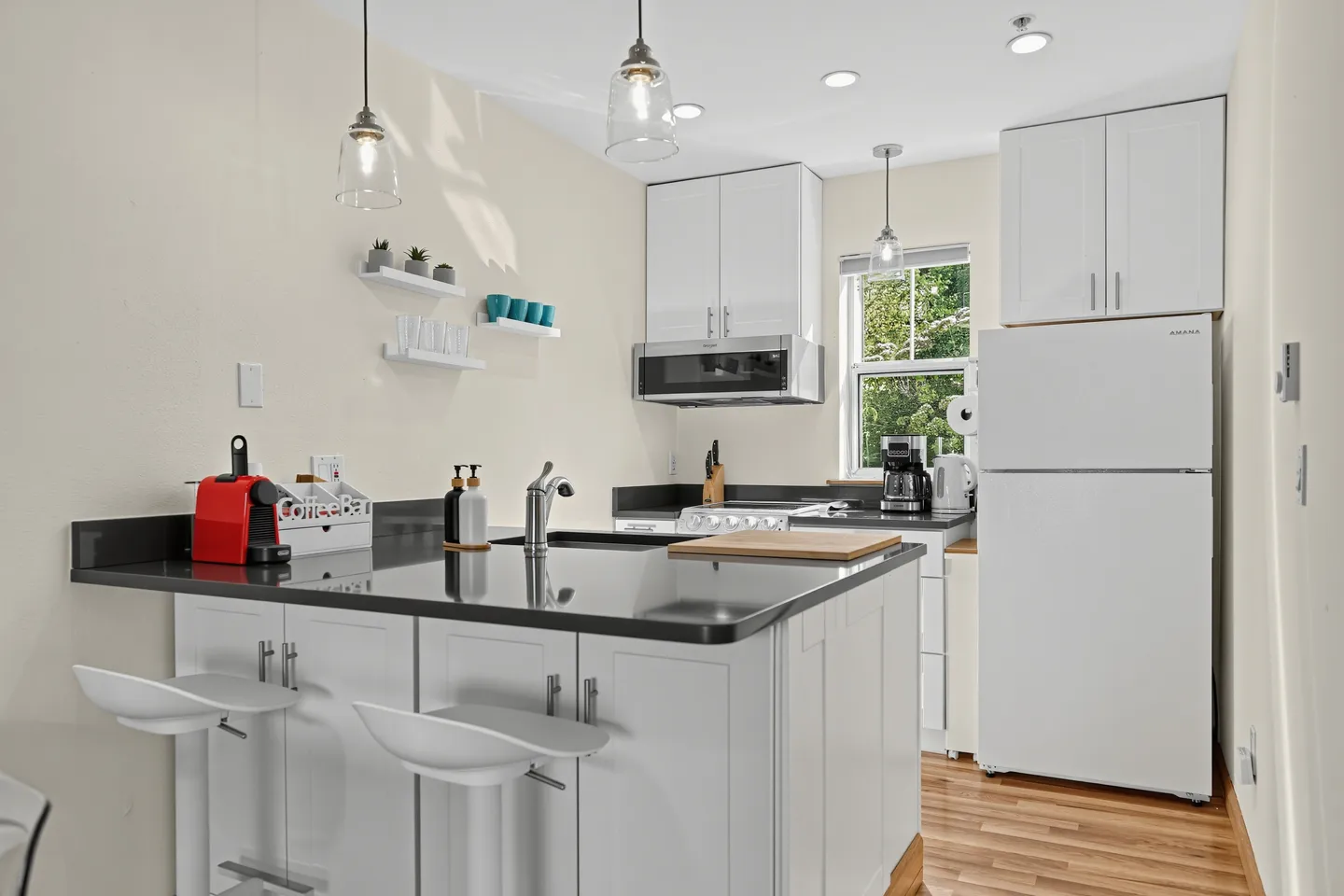 Compact kitchen featuring white cabinetry, dark countertops, an island with two barstools, and modern appliances.