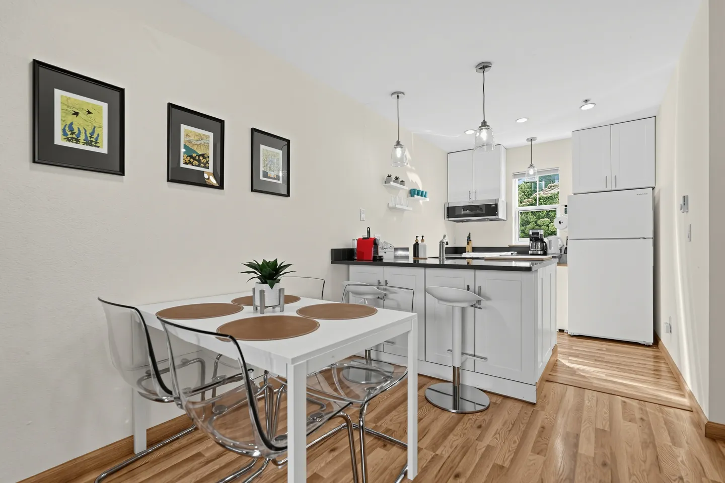 Dining area with a white table and clear chairs adjacent to an open kitchen with white cabinets.