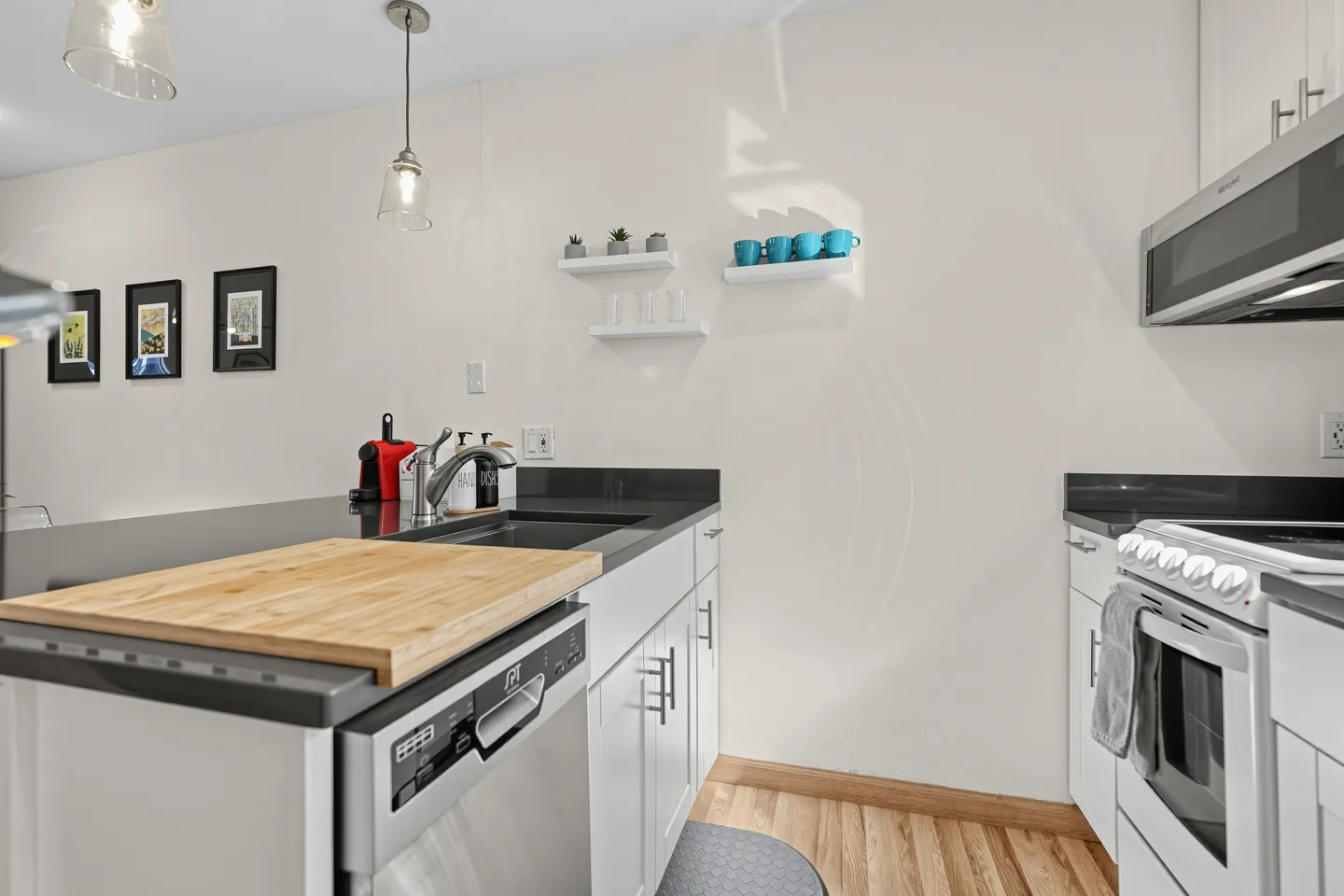 Kitchen counter with a sink, cutting board, dishwasher, and nearby white range and microwave.