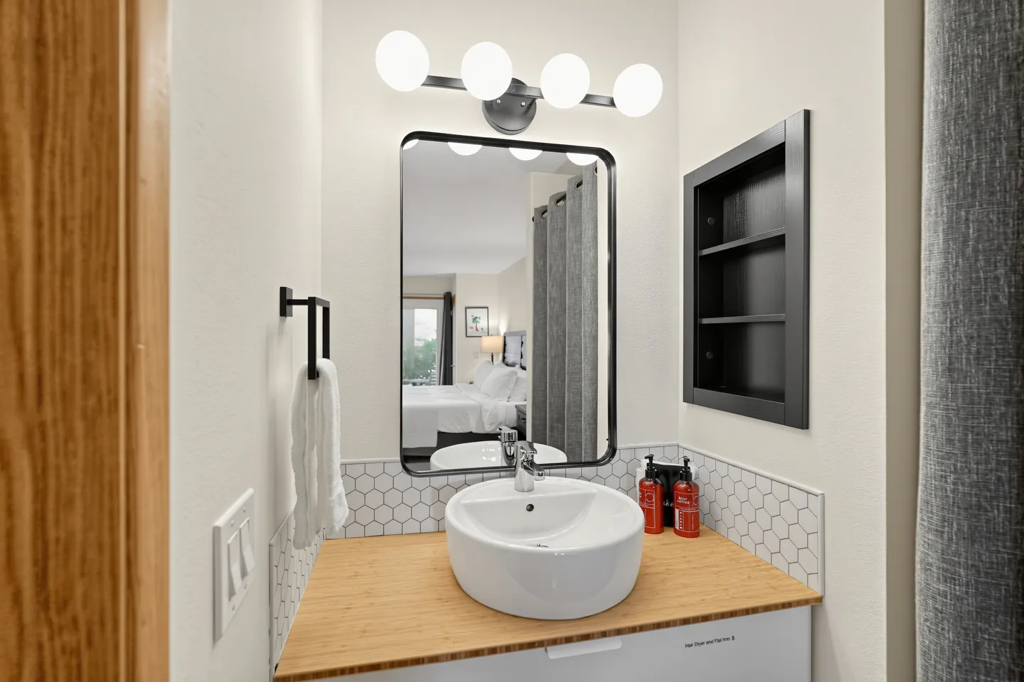 Bathroom vanity with a round vessel sink, wood-look countertop, rounded rectangular mirror, and modern globe vanity light.