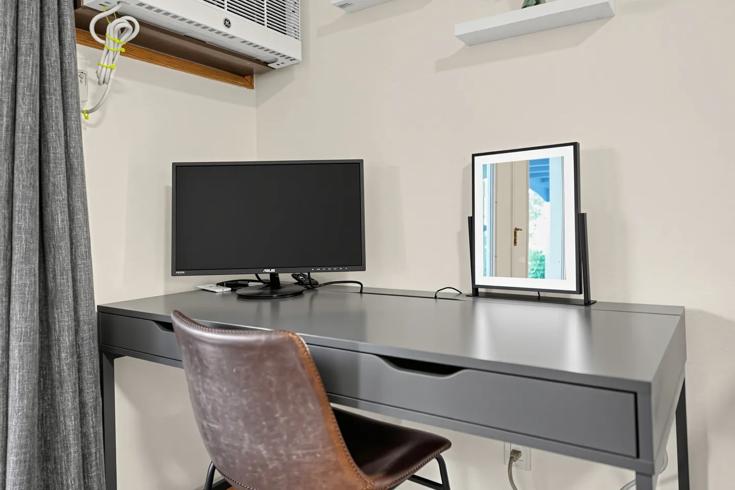 Dedicated workspace setup featuring a gray desk, brown leather chair, computer monitor, and vanity mirror.
