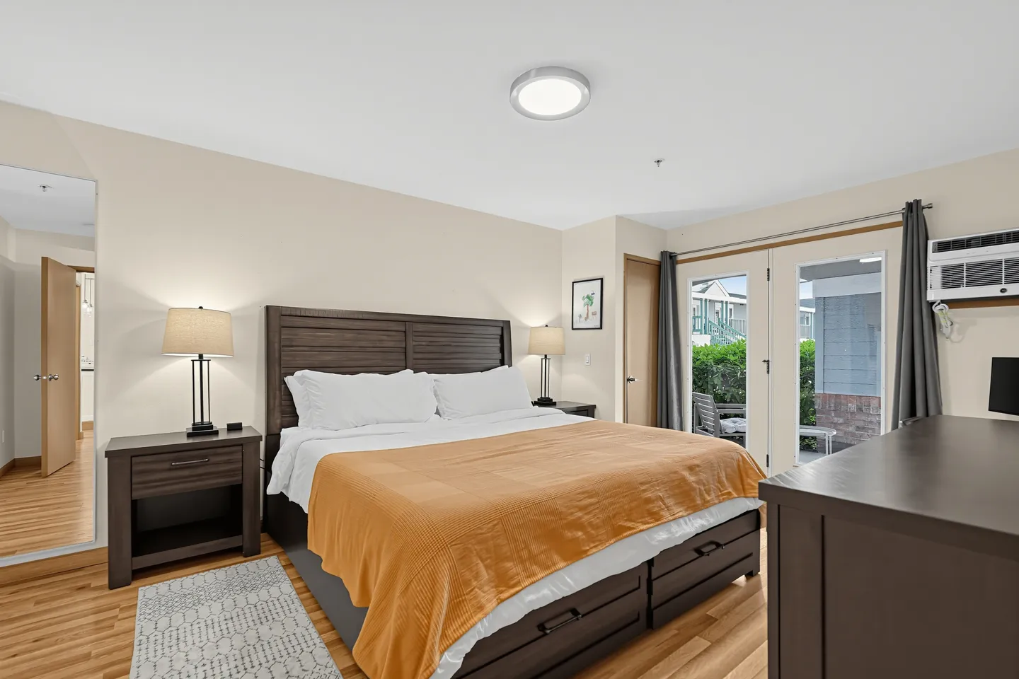 Bedroom with a large dark wood bed, matching nightstands with lamps, wood-style flooring, and glass doors leading outside.